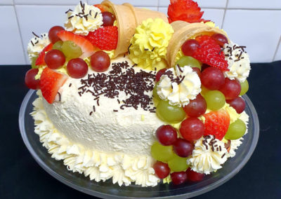 A birthday cake covered in cream, fresh fruit and chocolate sprinkles